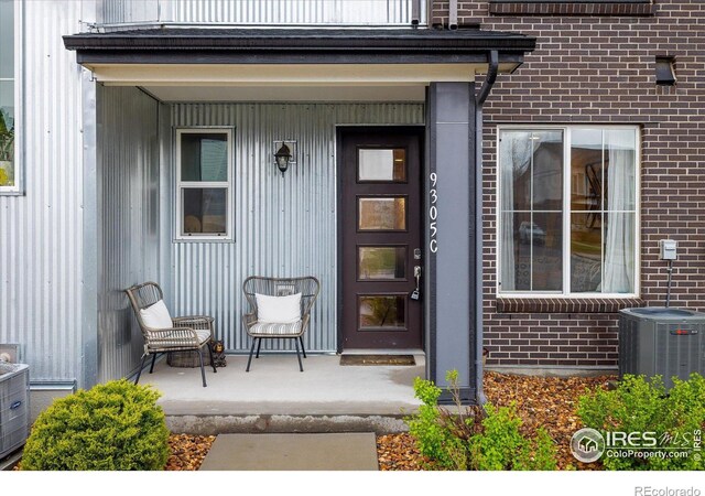 view of exterior entry featuring brick siding, cooling unit, and covered porch