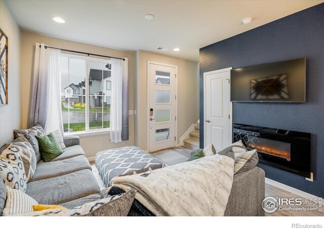 living room featuring baseboards, stairs, a glass covered fireplace, and recessed lighting