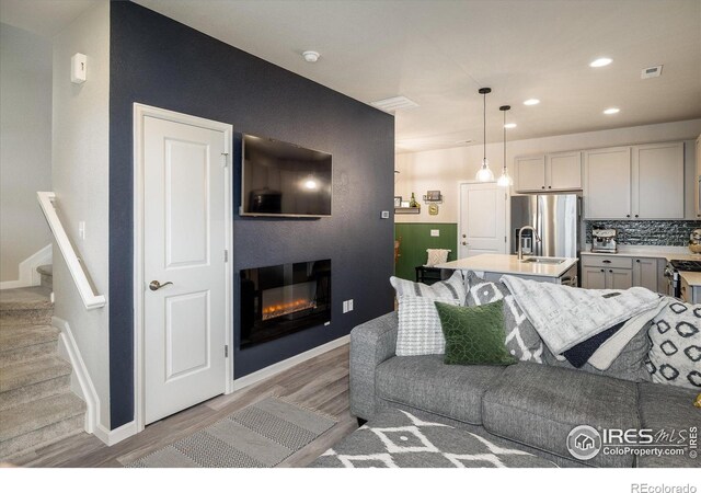 living room featuring light wood-style flooring, a glass covered fireplace, recessed lighting, stairs, and baseboards