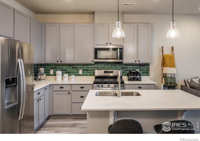 kitchen featuring stainless steel appliances, a kitchen breakfast bar, light wood finished floors, a sink, and light countertops