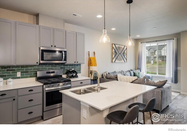 kitchen featuring stainless steel appliances, gray cabinetry, a sink, open floor plan, and light wood finished floors