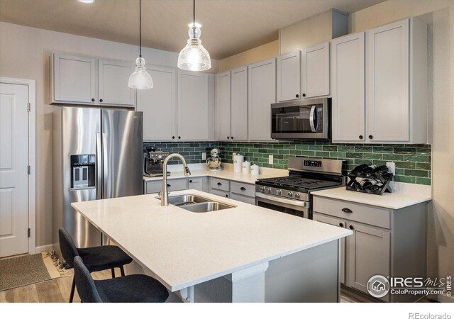 kitchen featuring stainless steel appliances, a sink, tasteful backsplash, light wood-type flooring, and a kitchen island with sink