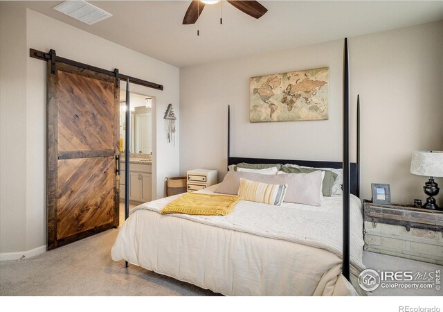 carpeted bedroom featuring a barn door, ensuite bath, and ceiling fan