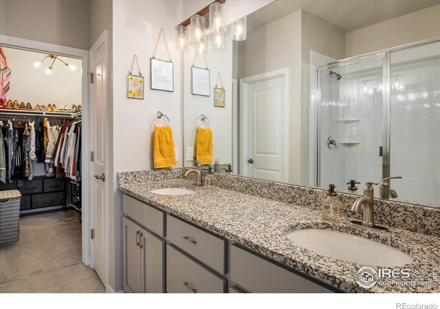 bathroom featuring a stall shower, double vanity, a walk in closet, and tile patterned flooring