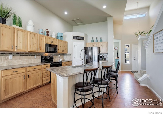 1318 Chamois Dr, Severance, CO 80550 - kitchen featuring a towering ceiling, a sink, black appliances, light brown cabinets, and a breakfast bar