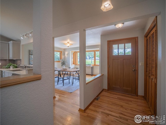 entryway with light wood-style flooring, track lighting, and baseboards