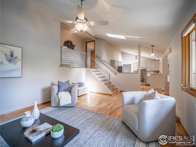 living area with vaulted ceiling, stairs, baseboards, light wood-style flooring, and a skylight