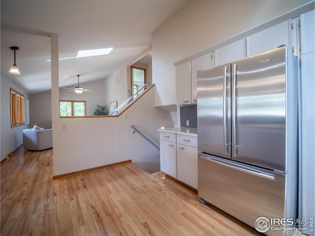 kitchen featuring stainless steel fridge, lofted ceiling, white cabinetry, light wood-style floors, and a skylight