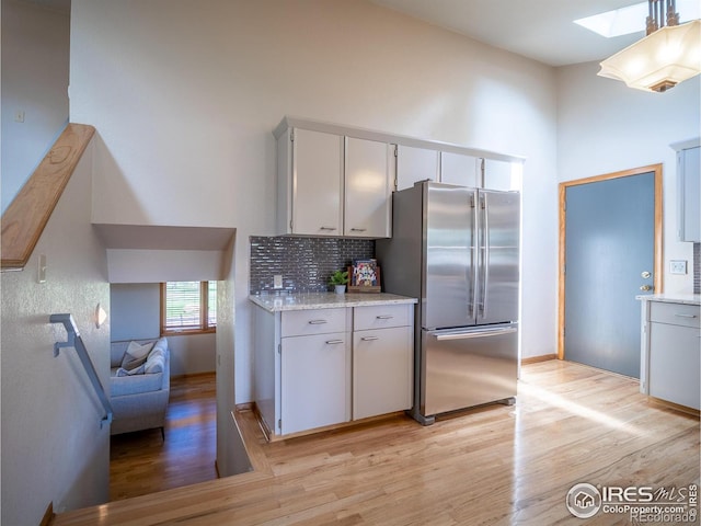 kitchen with freestanding refrigerator, a skylight, light wood-style flooring, tasteful backsplash, and a towering ceiling