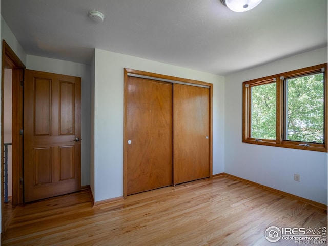 unfurnished bedroom featuring baseboards, a closet, and light wood-type flooring
