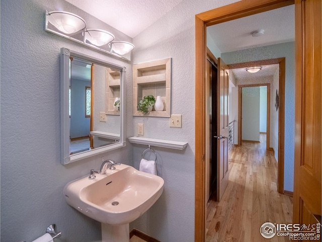 bathroom with a textured wall, wood finished floors, a sink, vaulted ceiling, and a textured ceiling