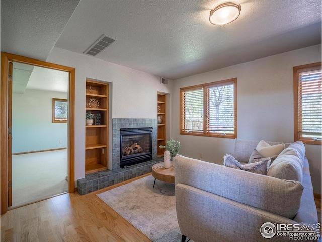 living room with wood finished floors, a textured ceiling, built in shelves, a tiled fireplace, and baseboards