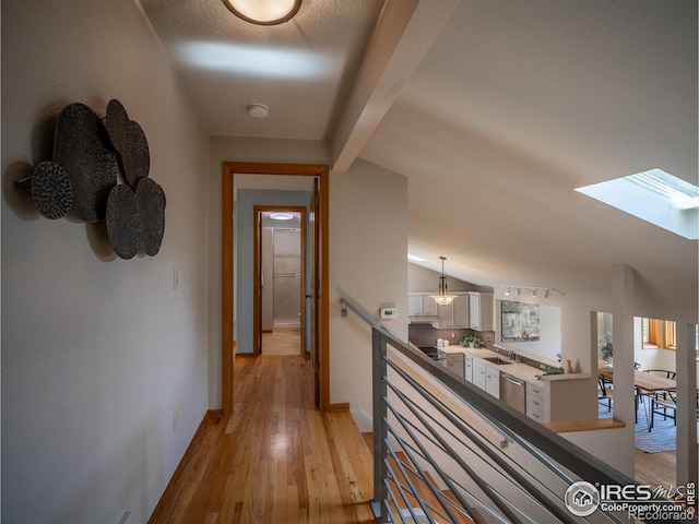 hall featuring an upstairs landing, light wood-type flooring, a sink, baseboards, and a skylight
