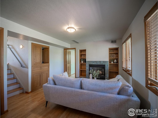 living area featuring a glass covered fireplace, light wood-style floors, built in shelves, stairway, and a textured ceiling