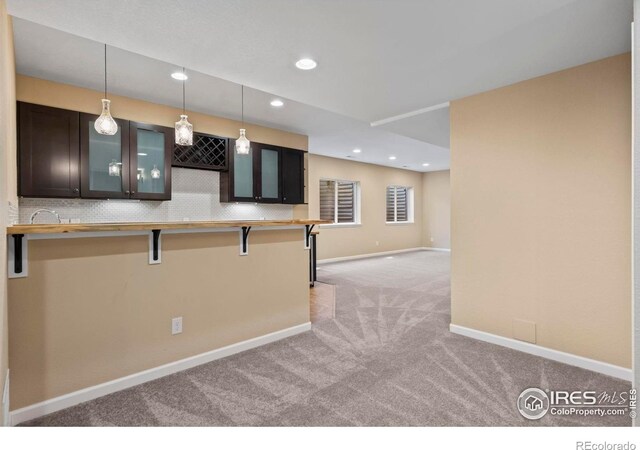 2458 Vale Way, Erie, CO 80516 - kitchen featuring light carpet, a kitchen bar, glass insert cabinets, hanging light fixtures, and baseboards