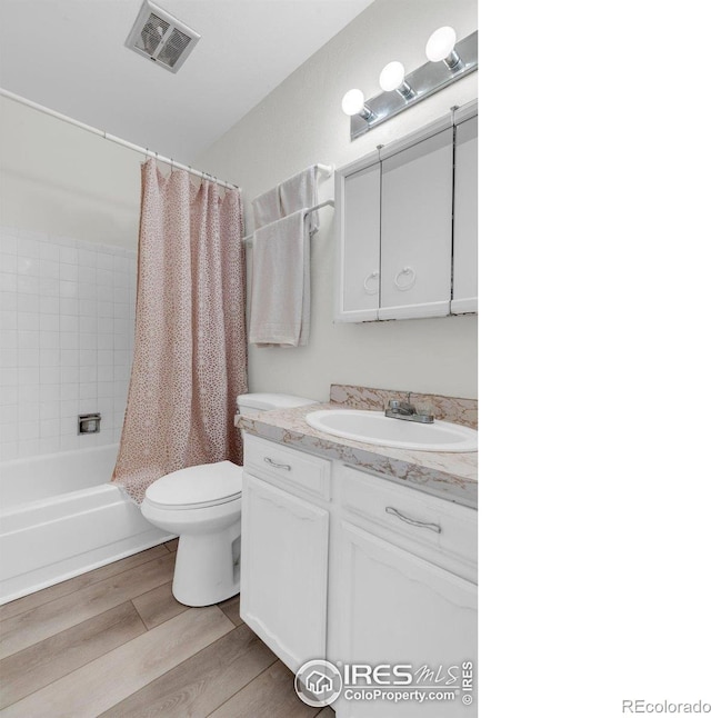 bathroom with toilet, wood finished floors, vanity, and shower / bath combination with curtain