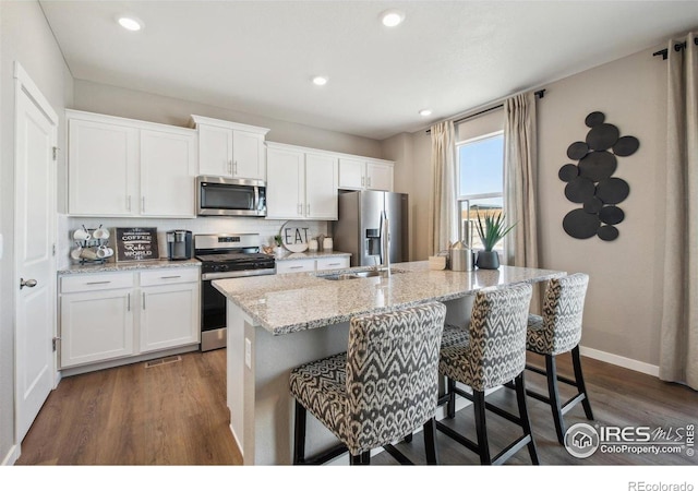 kitchen featuring appliances with stainless steel finishes, a kitchen island with sink, dark wood-style flooring, white cabinets, and recessed lighting
