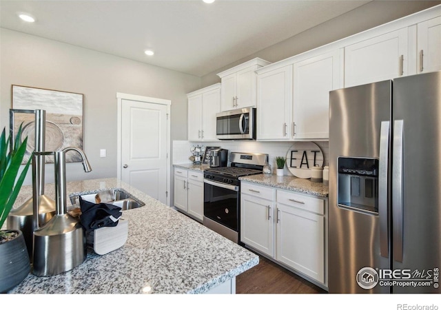 kitchen with stainless steel appliances, white cabinetry, a sink, backsplash, and light stone countertops