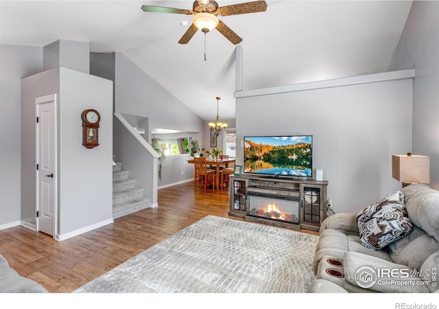 living room with wood finished floors, vaulted ceiling, a ceiling fan, stairway, and a chandelier