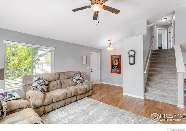 living room featuring ceiling fan, wood finished floors, stairs, baseboards, and vaulted ceiling