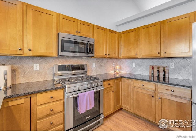 kitchen featuring stainless steel appliances, light wood-type flooring, dark stone counters, and tasteful backsplash