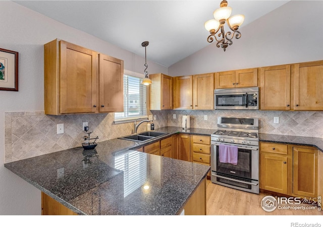 kitchen with stainless steel appliances, a sink, vaulted ceiling, a peninsula, and light wood-style floors