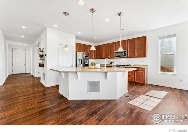 kitchen with stainless steel appliances, dark wood-type flooring, recessed lighting, a kitchen breakfast bar, and brown cabinetry