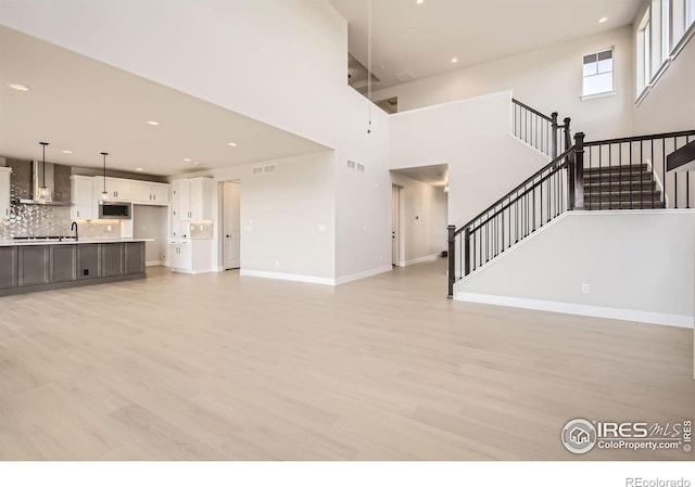 1679 Crystalline Dr, Windsor, CO 80550 - unfurnished living room featuring stairway, light wood-style floors, recessed lighting, baseboards, and a high ceiling