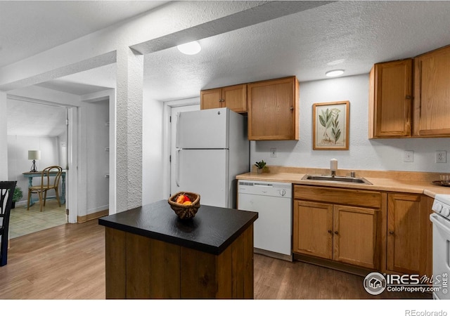 kitchen featuring white appliances, a sink, light wood finished floors, brown cabinets, and a textured ceiling