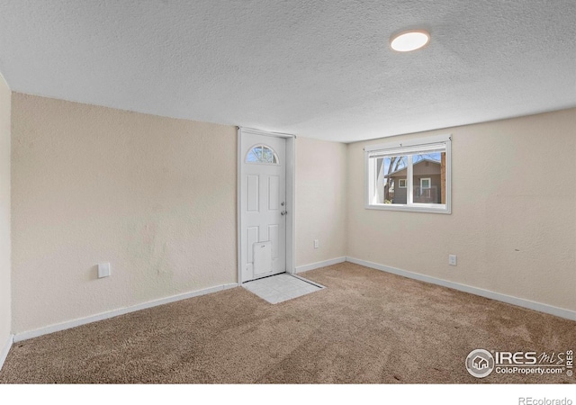 carpeted empty room featuring a textured ceiling and baseboards