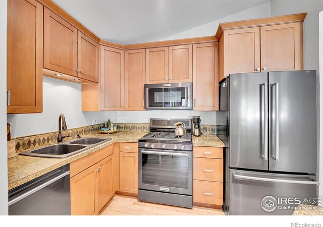 kitchen with appliances with stainless steel finishes, a sink, vaulted ceiling, light countertops, and light wood-type flooring