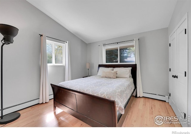 bedroom featuring a baseboard heating unit, vaulted ceiling, light wood-style floors, and multiple windows