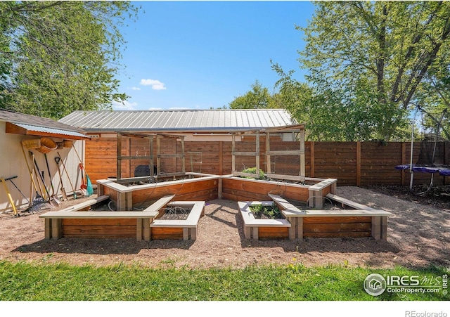 view of yard with a trampoline, fence, an outbuilding, and a garden