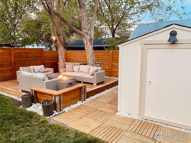 view of patio with an outdoor living space with a fire pit, a wooden deck, a storage shed, a fenced backyard, and an outbuilding