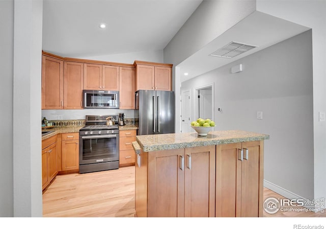 kitchen featuring appliances with stainless steel finishes, lofted ceiling, light countertops, light wood-style floors, and a center island