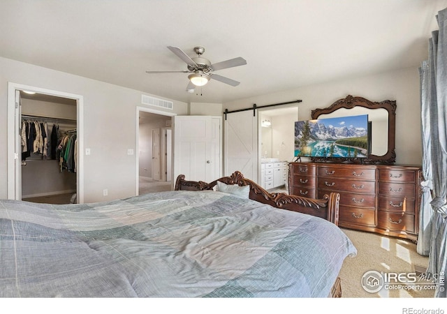 bedroom with a barn door, a spacious closet, a ceiling fan, light colored carpet, and ensuite bath