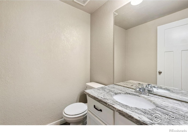 half bathroom with vanity, a textured wall, and toilet