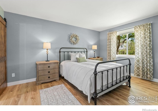 bedroom featuring wood finished floors, a barn door, and baseboards