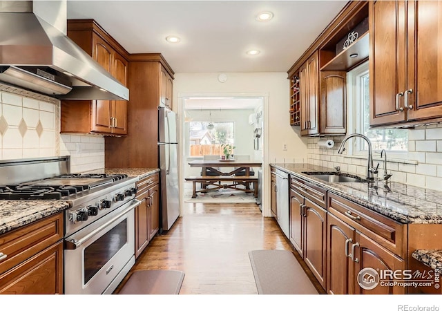 1136 Venice St, Longmont, CO 80501 - kitchen with stainless steel appliances, wall chimney range hood, a sink, light wood finished floors, and stone counters