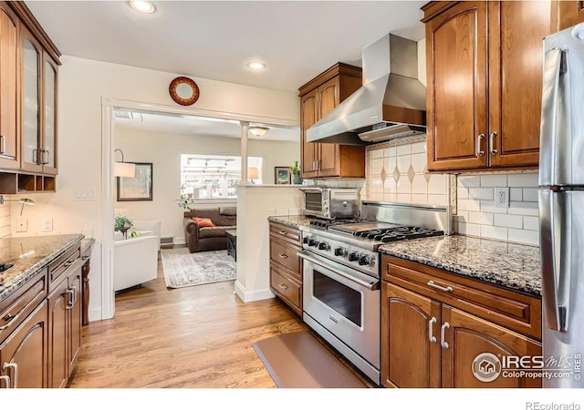 1136 Venice St, Longmont, CO 80501 - kitchen with stainless steel appliances, wall chimney exhaust hood, light wood-type flooring, dark stone countertops, and recessed lighting
