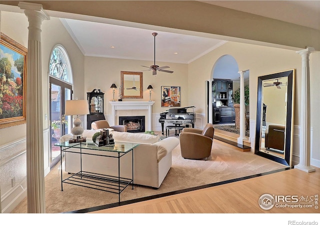 living area with decorative columns, ceiling fan, light wood-style flooring, a fireplace, and crown molding