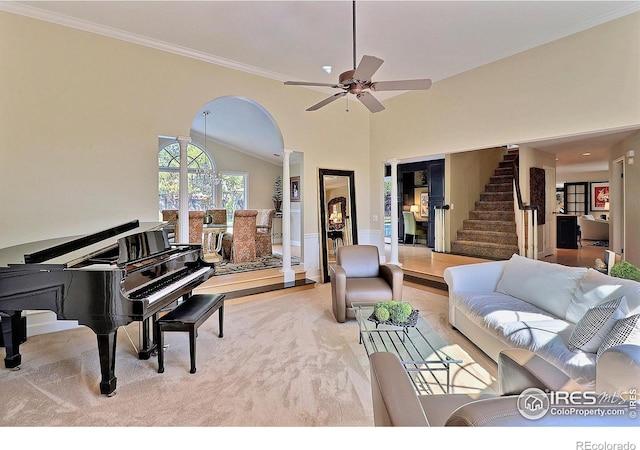 living room featuring a ceiling fan, crown molding, stairs, arched walkways, and light colored carpet