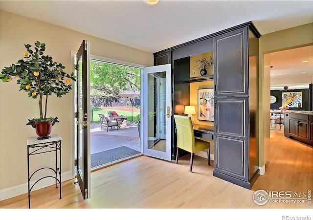 doorway with light wood-style flooring, a desk, and baseboards