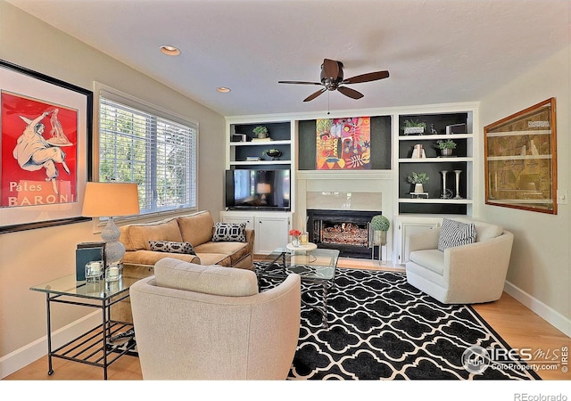 living room featuring a high end fireplace, baseboards, wood finished floors, a ceiling fan, and built in shelves