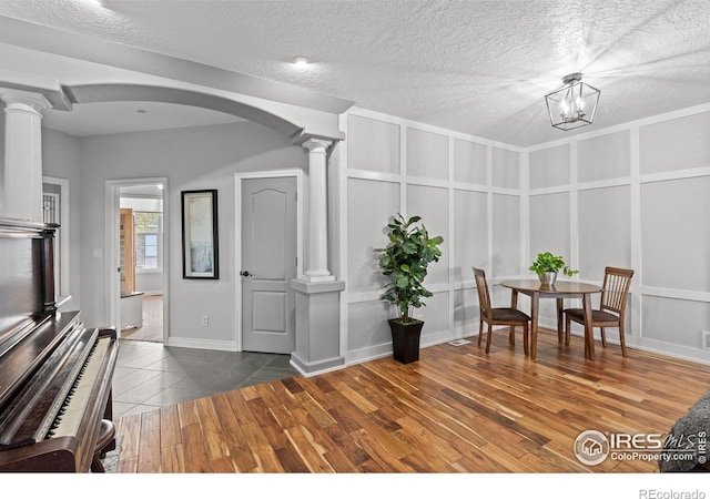 dining room featuring decorative columns, arched walkways, wood finished floors, a textured ceiling, and baseboards
