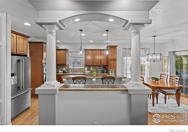 kitchen featuring high quality fridge, ornate columns, a kitchen island, brown cabinets, and decorative backsplash