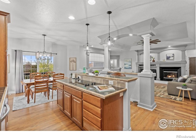 kitchen featuring decorative columns, light wood-style floors, brown cabinetry, a lit fireplace, and pendant lighting