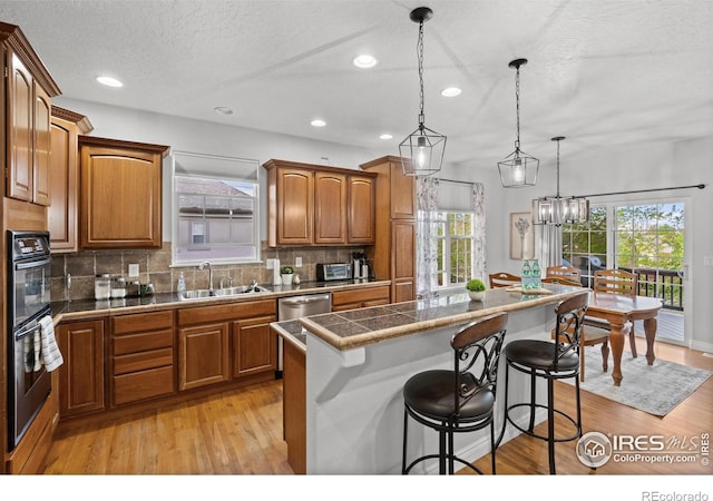 kitchen with a sink, brown cabinets, a kitchen island, light wood-type flooring, and a textured ceiling