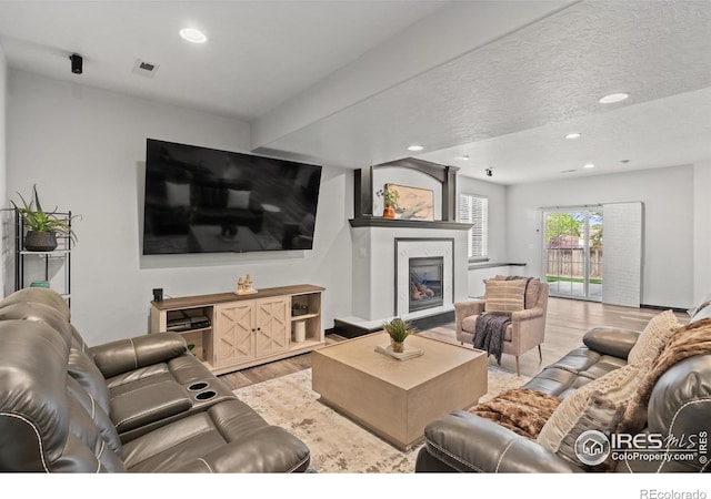 living area with light wood-style floors, a fireplace, recessed lighting, and a textured ceiling