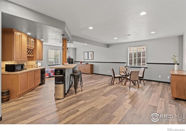 kitchen with black microwave, light wood-style floors, glass insert cabinets, recessed lighting, and light countertops